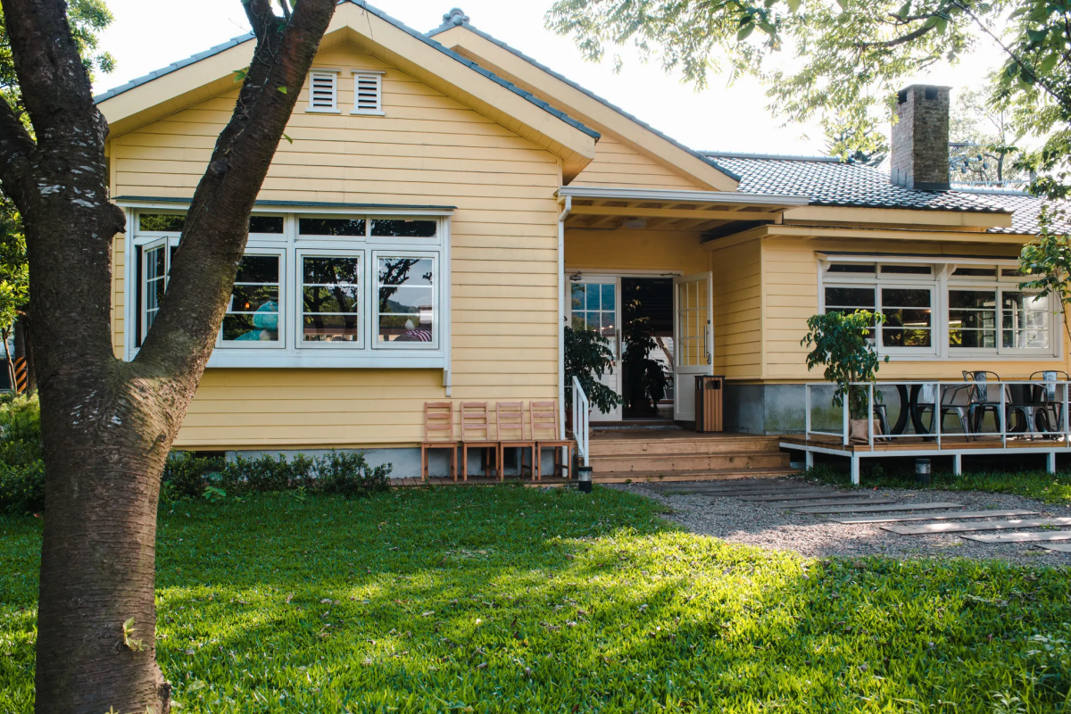 Exterior photo of yellow single-story house with front porch, lawn, and large windows.