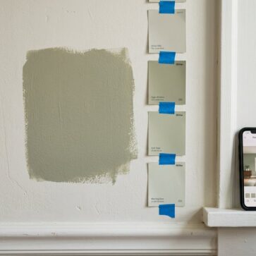 Paint swatches and a phone running a paint color visualizer app against a partly painted wall